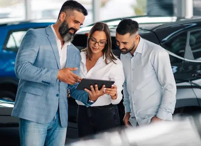 Two customers and a car dealer look at a tablet together in the showroom.