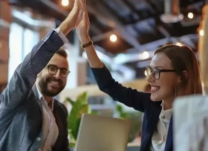 People sitting in a meeting. Two of them happily give each other a high five.