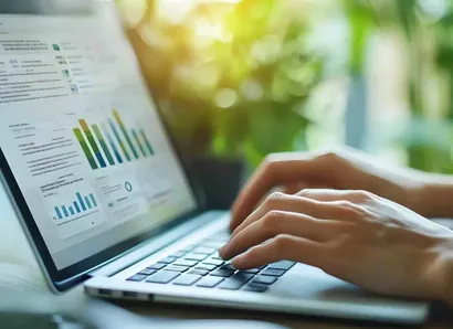 A person works on data on a laptop in an office equipped with green plants.