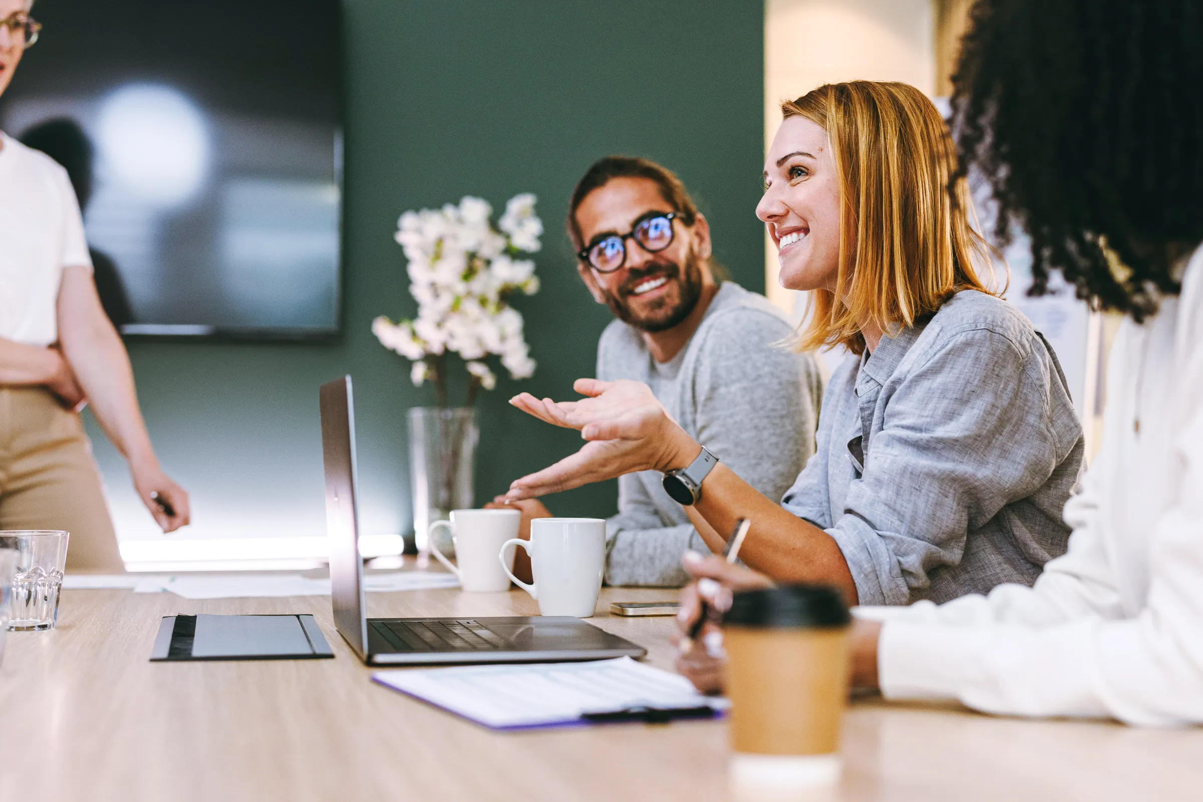 People in a business meeting, a smiling woman speaks while colleagues listen.